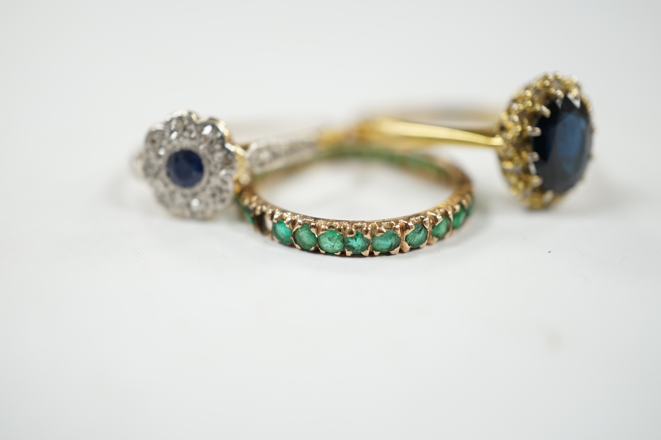 A 1920's 18ct and plat, sapphire and diamond set flower head cluster ring, size L, a 1960's 18ct gold sapphire and diamond set oval cluster ring and a yellow metal and emerald chip set full eternity ring, gross weight 6.